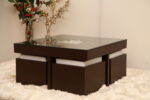 Modern glass-top center table with dark wooden base and 4 puffies, designed for compact living spaces.