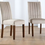 Two velvet upholstered dining chairs with vertical tufted stitching and wooden legs placed on a wooden floor.