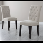 Set of two elegant button-tufted dining chairs with soft upholstery and solid wooden legs in a modern room.