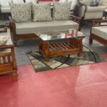 Classic wooden sofa set with floral-patterned cushions, a glass-top center table, and matching puffy.